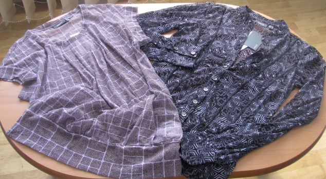 Dwie bluzki damskie, jedna w kratkę brązowo-białą z krótkim rękawem, druga wzorzysta czarno-biała z długim rękawem, leżące na okrągłym drewnianym stole.